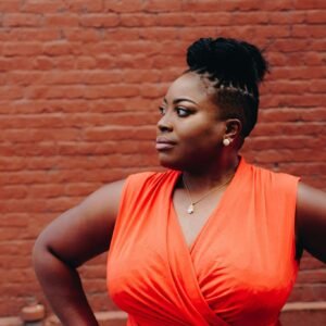 Portrait of a confident woman in a red dress posing against a brick wall.